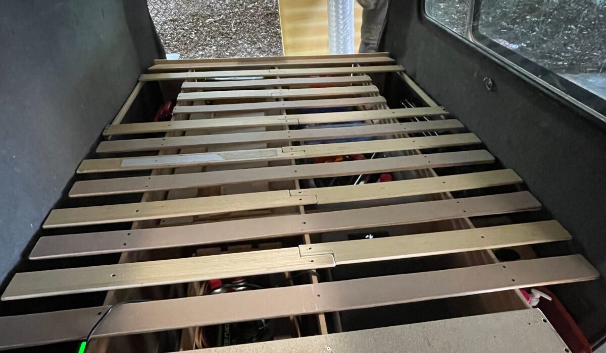 Der Lattenrost gefällt uns so sehr gut. Links und rechts gibt es zwei Stauräume für Sachen, an die wir nicht oft ran müssen und durch eine Klappe unter der Matratze geöffnet werden können. Im vorderen Bereich haben wir eine stabile Holzplatte verschraubt, damit wir dort gut sitzen können.